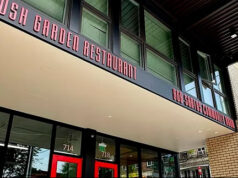 Front view of Bush Garden Restaurant with red doors and large glass storefronts on a sunny street corner.