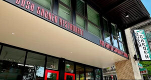 Front view of Bush Garden Restaurant with red doors and large glass storefronts on a sunny street corner.