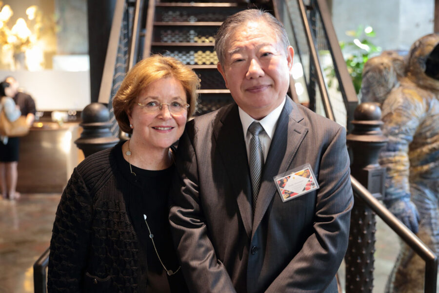 _-5 | Seattle’s Japanese Community News – North American Post Smiling man in a gray suit and woman with glasses stand together indoors at a formal event near a staircase.