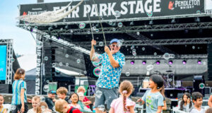 A performer on a stage entertaining a group of children with bubbles at an outdoor festival.