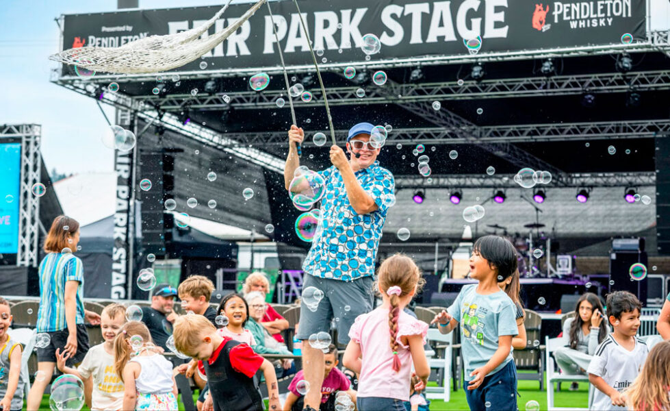 A performer on a stage entertaining a group of children with bubbles at an outdoor festival.
