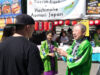 Festival scene with people in green traditional jackets at a Japanese food stall decorated with red lanterns and banners advertising Hachinohe Aomori Japan on a sunny day (informative)