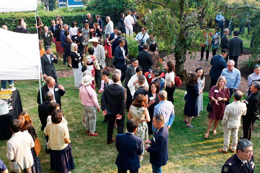 Group of adults mingling at an outdoor garden reception, dressed in business or smart-casual attire.