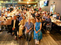 Farewell to Consul General and Mrs. Iyori Large group photo of diverse people seated and standing around long restaurant tables for a group portrait.