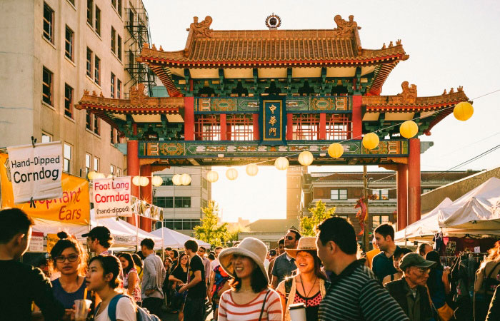 Crowd at a Chinatown festival under a colorful Chinese gate with food stalls and lanterns.