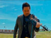 Man in a suit playing a violin outdoors in a grassy field under a bright blue sky