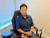 Man in a blue shirt sits in a specialized therapy chair, with a leg compression/cooling device strapped to his right leg and connected control panels nearby.