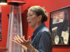 Woman speaking and gesturing with hands in a red-walled room, giving a presentation or talk.
