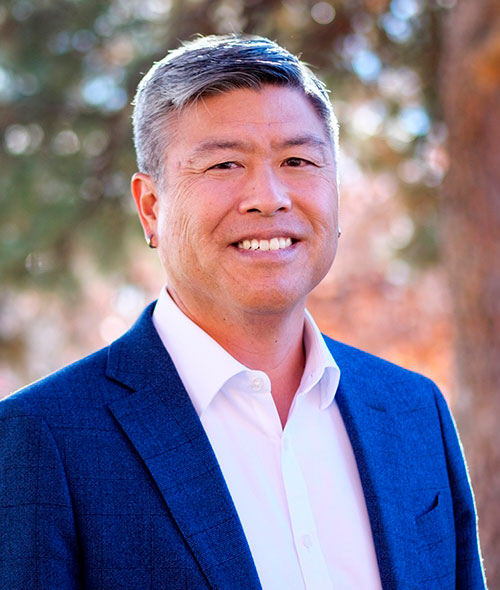 Head-and-shoulders portrait of a man in a blue suit smiling outdoors